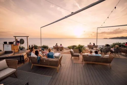 Menschen genießen eine Mahlzeit auf der Terrasse im 7Pines Resort Ibiza, kulinarische Exzellenz am Wasser.