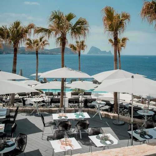Strandseite des 7Pines Resort Ibiza mit Tischen und Sonnenschirmen, verkörpert das Wesen der INFINITY POOL BAR.