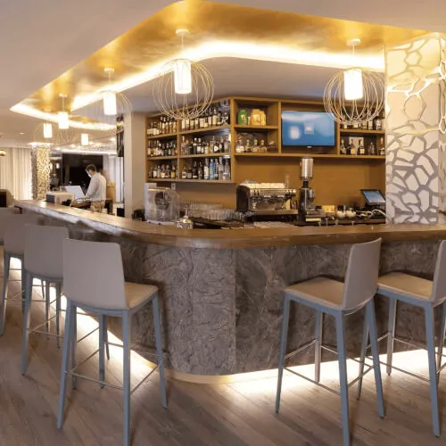 Lobby Bar & Lounge im 7Pines Resort Ibiza mit einer Bar und Stühlen am Tresen.