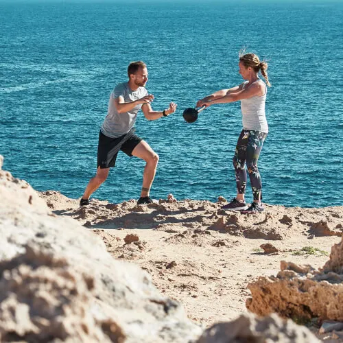 Pareja jugando con un balón en la playa de 7Pines Resort Ibiza, disfrutando del verano y el fitness.