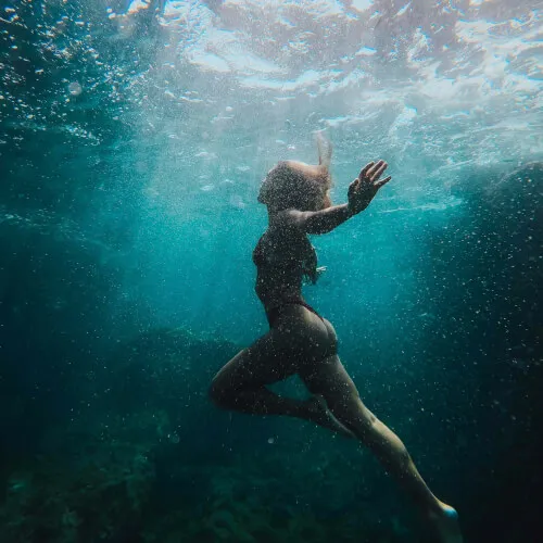 Mujer buceando bajo el agua en 7Pines Resort Ibiza, una experiencia de retiro serena.